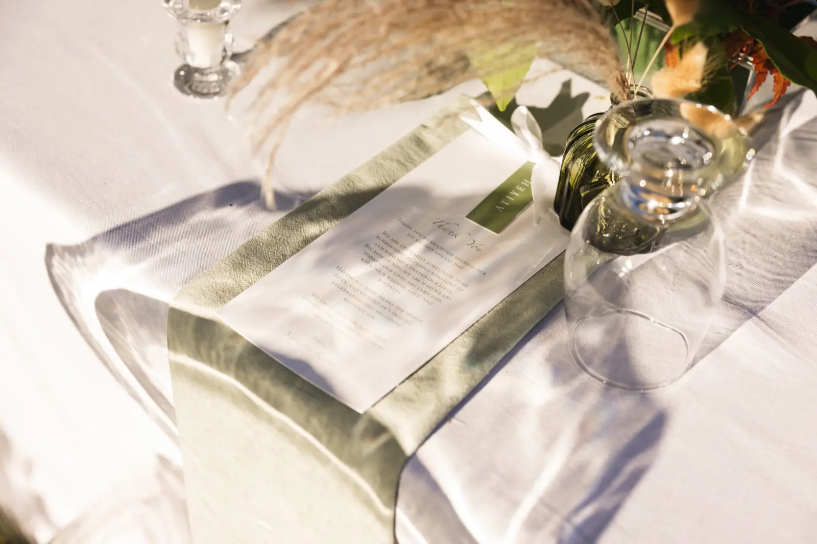 Sage napkin, printed menu and glassware on a white table in evening light